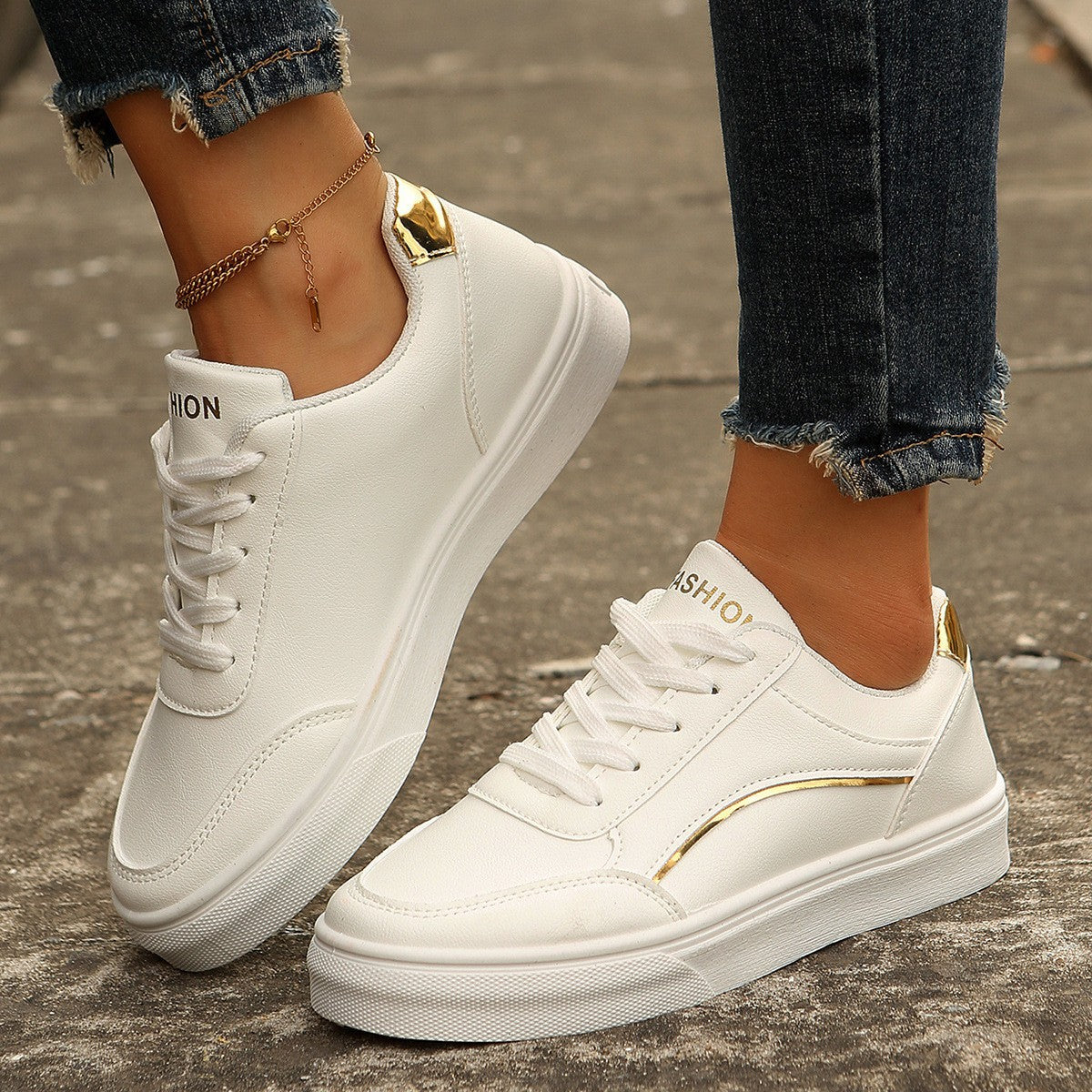 White sneakers with gold accents worn by a person on a concrete surface